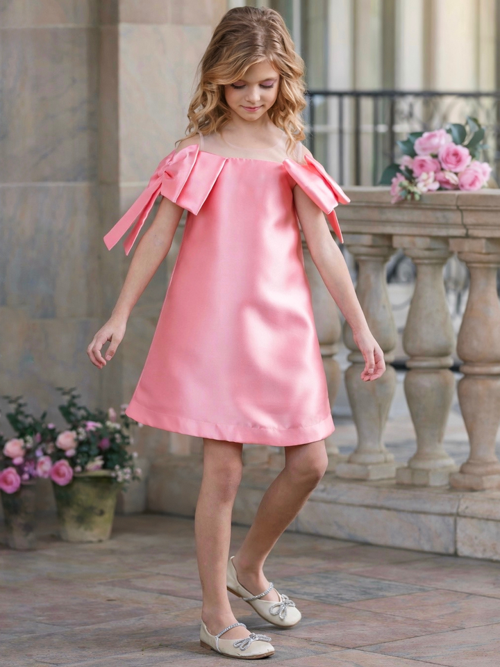 Girl wearing a blush pink satin shift dress with oversized shoulder bows, perfect for graduation, Easter, church, and spring pictures