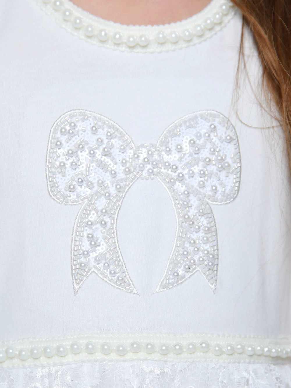 Close up of pearl trim neckline and bow on girls ivory dress