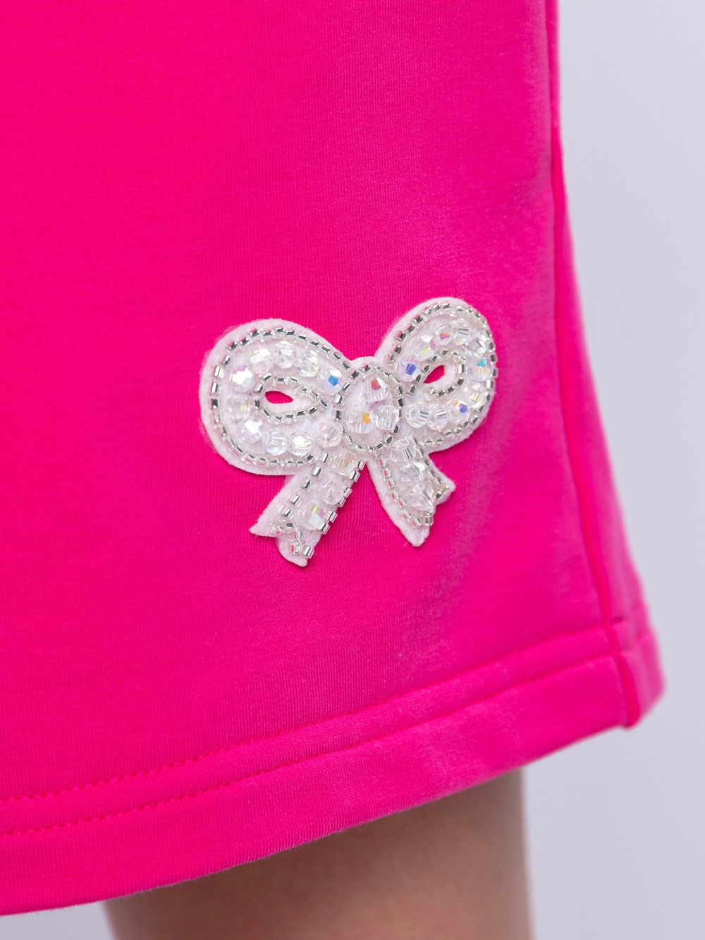 Pink fabric romper detail showing embellished bow patch