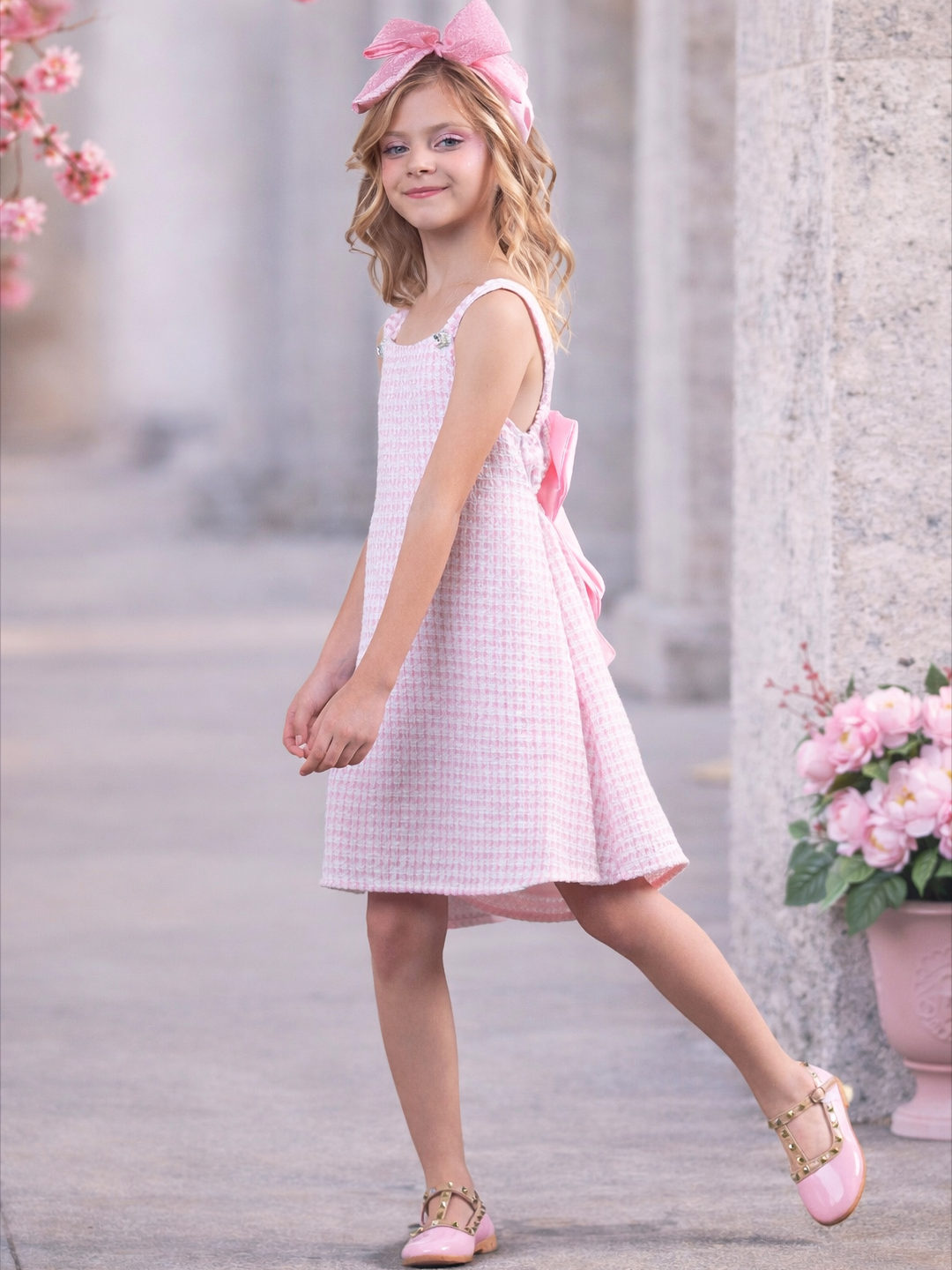 Little girl wearing a light pink tweed sleeveless shift dress with textured fabric and embellished shoulder straps, styled with a bow headband and pink Mary Jane shoes, perfect for Easter, graduation, spring pictures, church, and recitals.