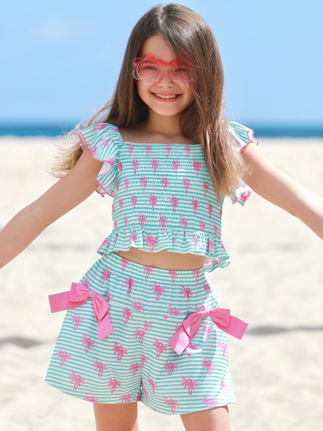 girl wearing mint stripe summer short set with palm print and bows