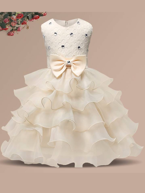Baby princess dress has a floral lace bodice with rhinestone details, a bow belt at the waist, and a multi-layered tulle skirt-creme