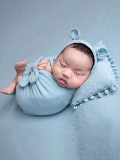 Baby features a shawl - wrap that has knots in the front with a cap with ears and a little pillow - blue