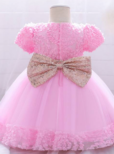 Baby dress has a floral bodice, a tulle skirt with floral hem, and a gold sequin belt with bow at the front and back