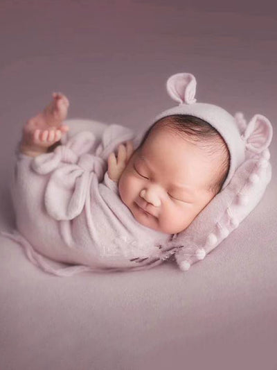 Baby features a shawl - wrap that has knots in the front with a cap with ears and a little pillow - pink