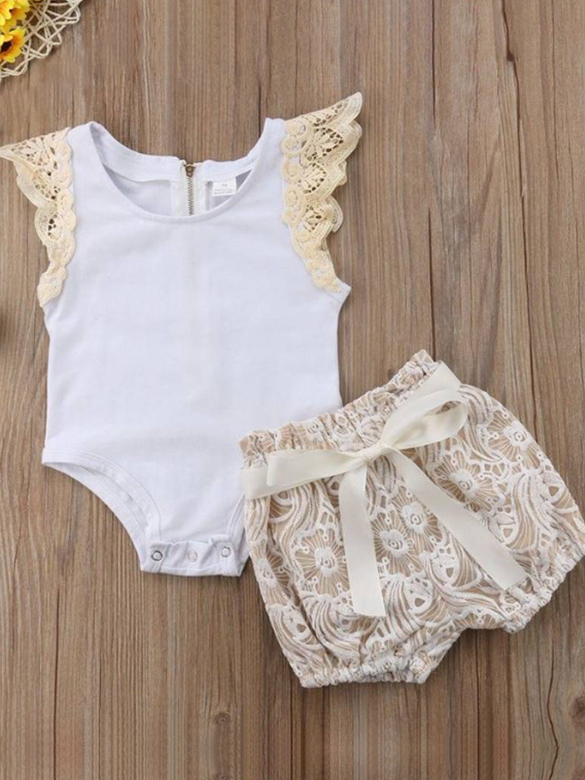 Baby set features a short-sleeved onesie with a crochet ruffle at the shoulder and embroidered shorts with a sash