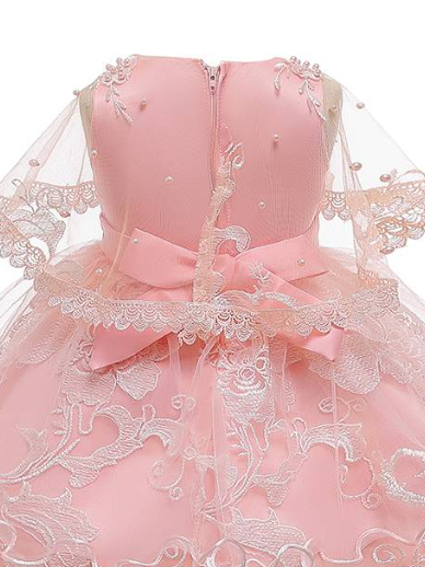 Girls satin dress has an embroidered tulle overlay with flower applique and pearl details. The dress has a tulle capelet and a large bow on the back