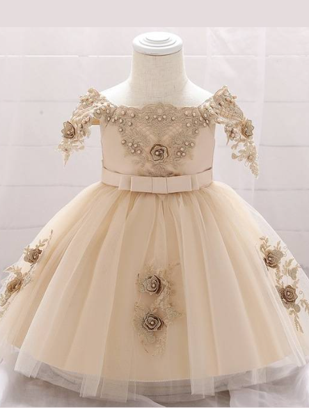 Baby dress has a satin embroidered bodice with pearl details and capped sleeves, a bow belt at the waist, and a tulle skirt with flower applique