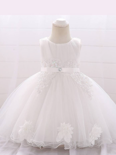 Baby dress has a tulle overlay with flower applique and a satin belt with rhinestone detail-white