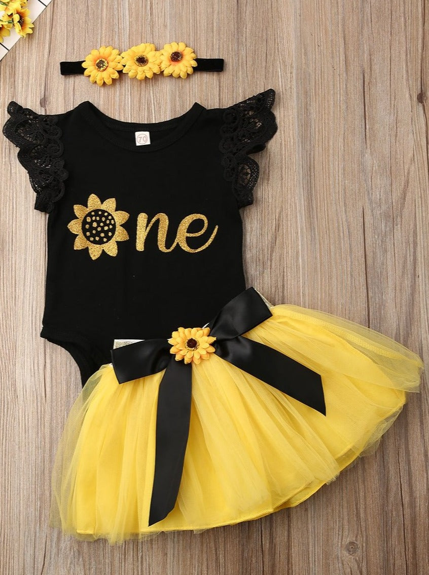 Baby set has a onesie with ruffled lace sleeves and "One" printed, a tutu skirt with sunflower sash, and a matching sunflower headband