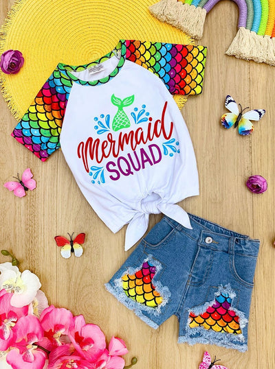 Girls Summer set features a rainbow mermaid scale raglan sleeve knot hem "Mermaid Squad" graphic tee with matching patched distressed denim shorts 2T to 12Y