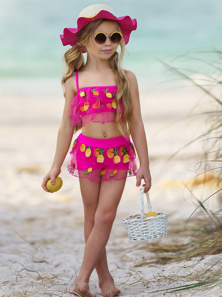 Two-piece hot pink swimsuit features ruffle and short bottoms with sheer ruffles and pineapple and lemon applique 4T-10Y