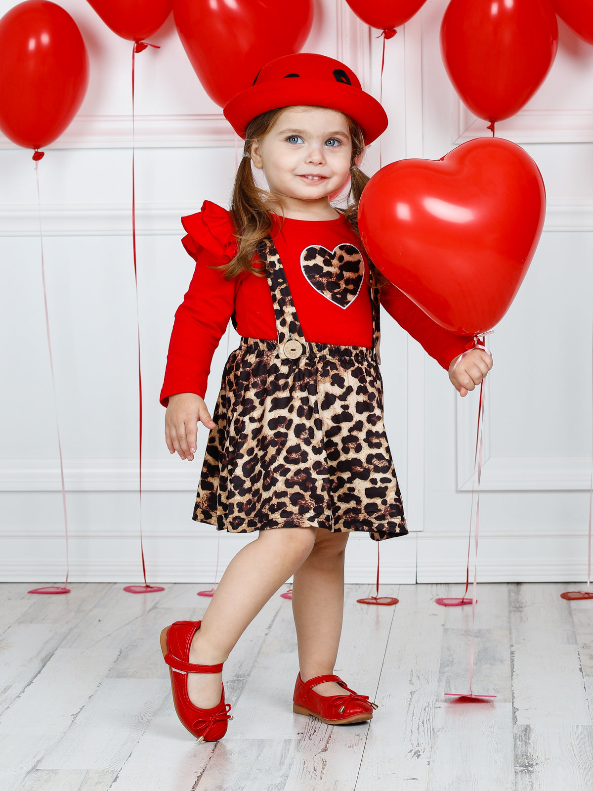 Girls Valentine two-piece set features a red long sleeve ruffle shoulder top with leopard print heart and leopard overall ruffle skirt with buttoned suspenders 