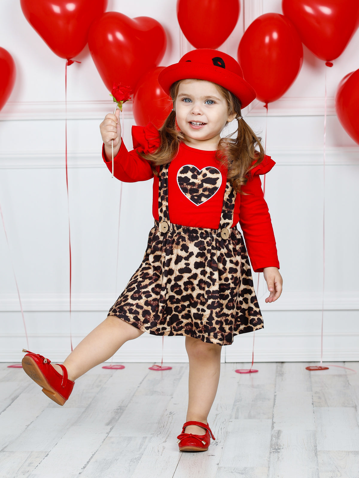Girls Valentine two-piece set features a red long sleeve ruffle shoulder top with leopard print heart and leopard overall ruffle skirt with buttoned suspenders 