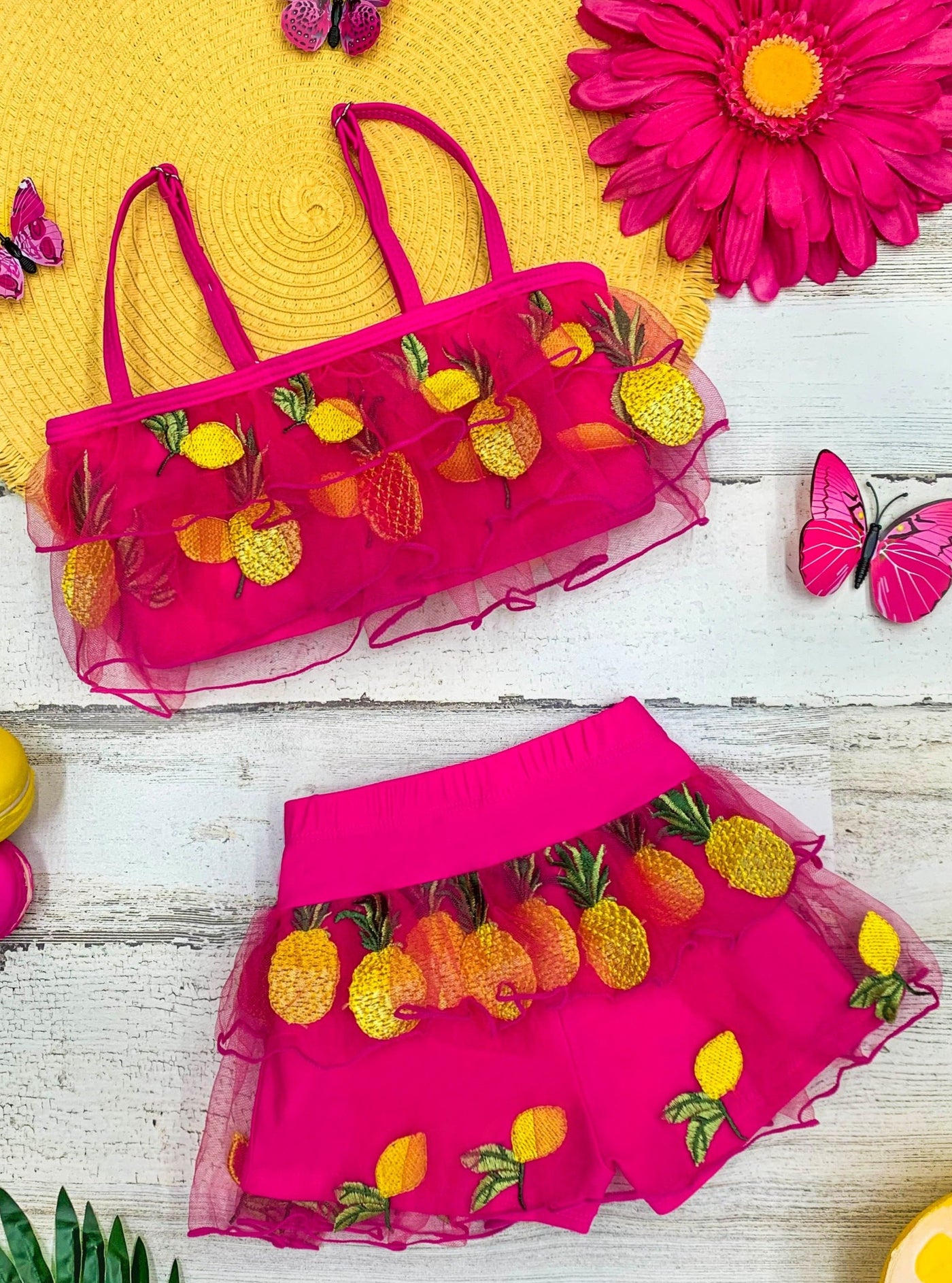 Two-piece hot pink swimsuit features ruffle and short bottoms with sheer ruffles and pineapple and lemon applique 4T-10Y