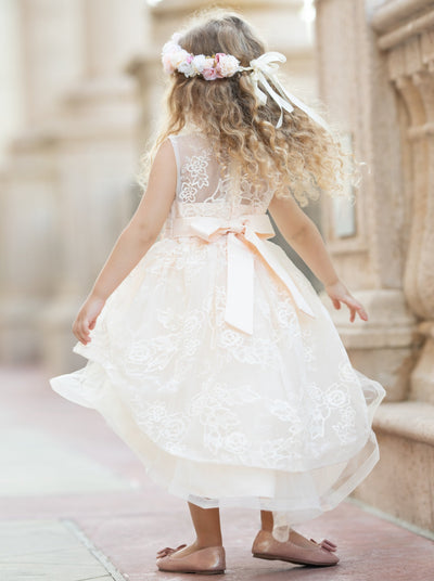 Girls hi-low and double layered dress has an embroidered bodice with pearl detail and bow belt
