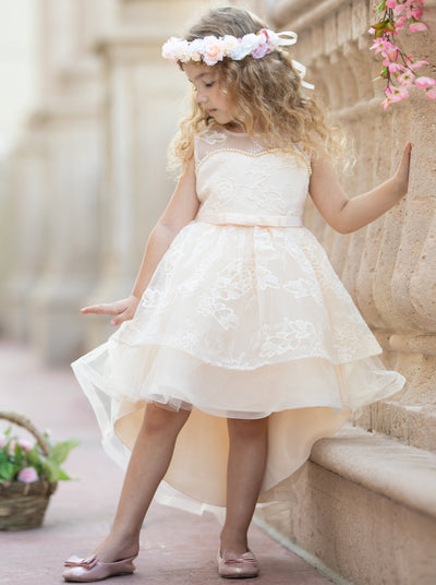 Girls hi-low and double layered dress has an embroidered bodice with pearl detail and bow belt