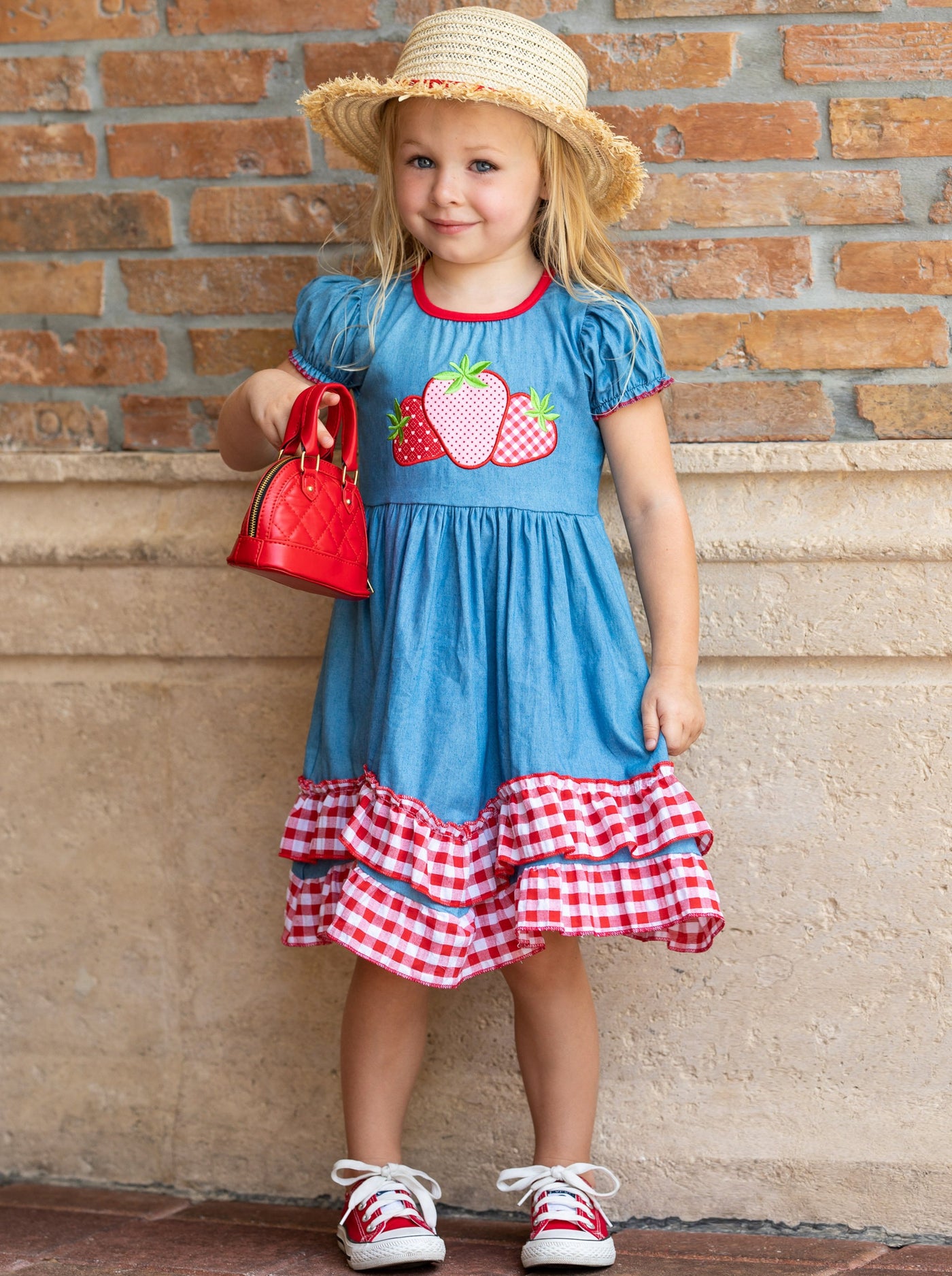 girls denim dress has a strawberries applique and red and white plaid ruffles