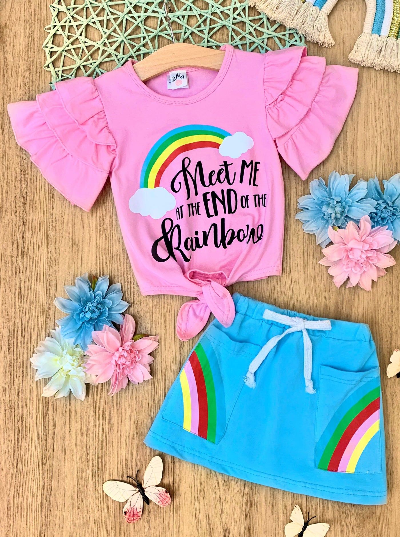 Girls set features a pink knot hem top with multi-layer ruffled sleeves and "Meet me at the end of the rainbow" graphic print and a blue skirt with built-in drawstrings and rainbow front pockets