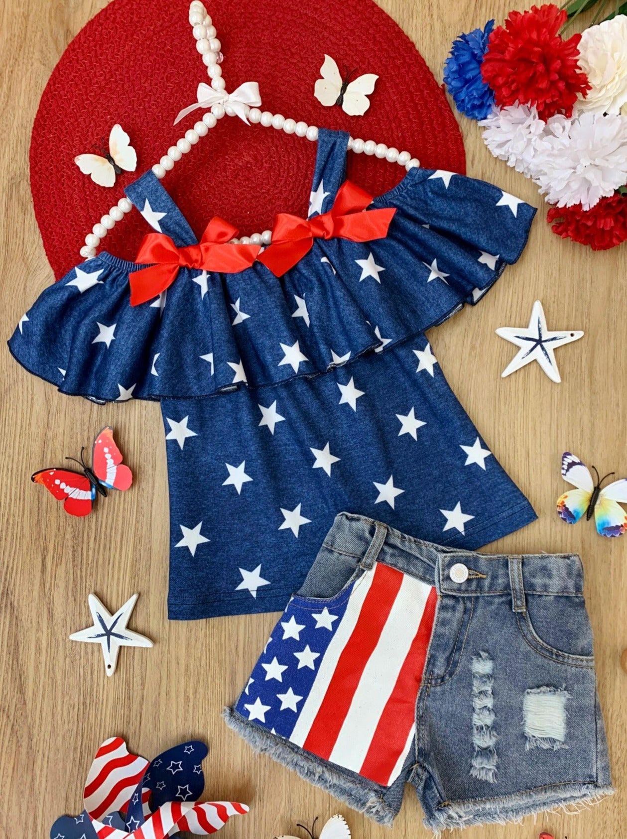 Girls 4th of July set features a blue cold-shoulder top with white stars with frayed denim shorts with flag patch