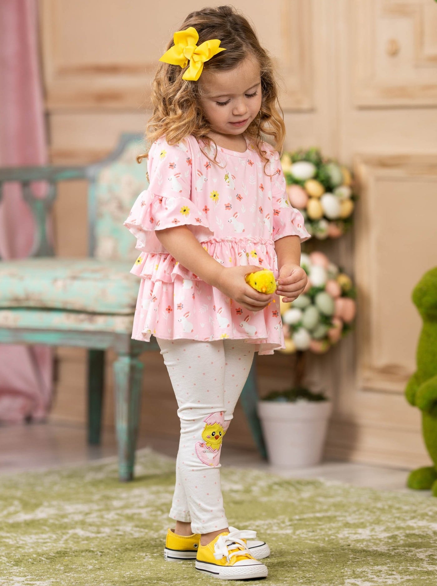 Girls Easter-themed set features a pink ruffled top with chick and bunny print and white polka dot leggings with hatching chick patches on the knees for 2T to 10Y toddlers and girls