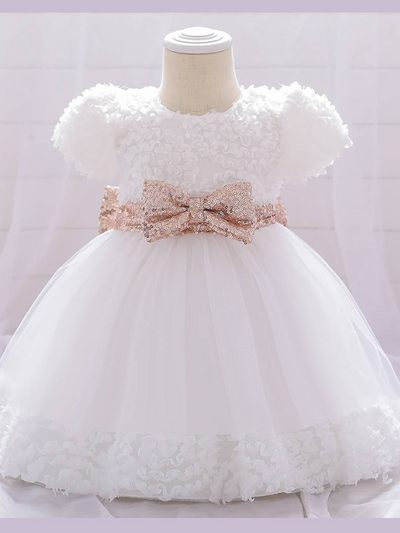 Baby dress has a floral bodice, a tulle skirt with floral hem, and a gold sequin belt with bow at the front and back