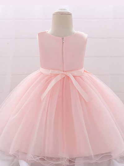 Baby dress has a tulle overlay with flower applique and a satin belt with rhinestone detail-pink